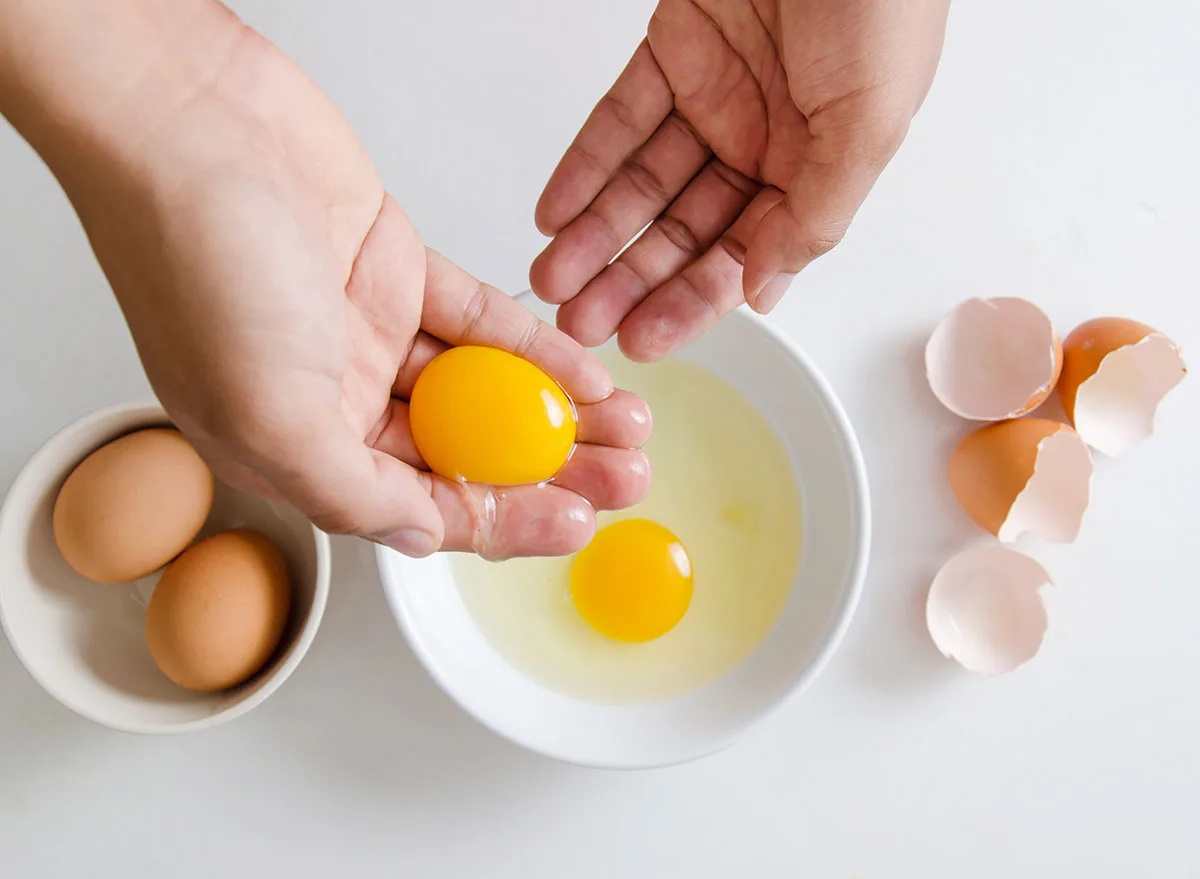frau hält ein eigelb in der hand neben anderen eiern