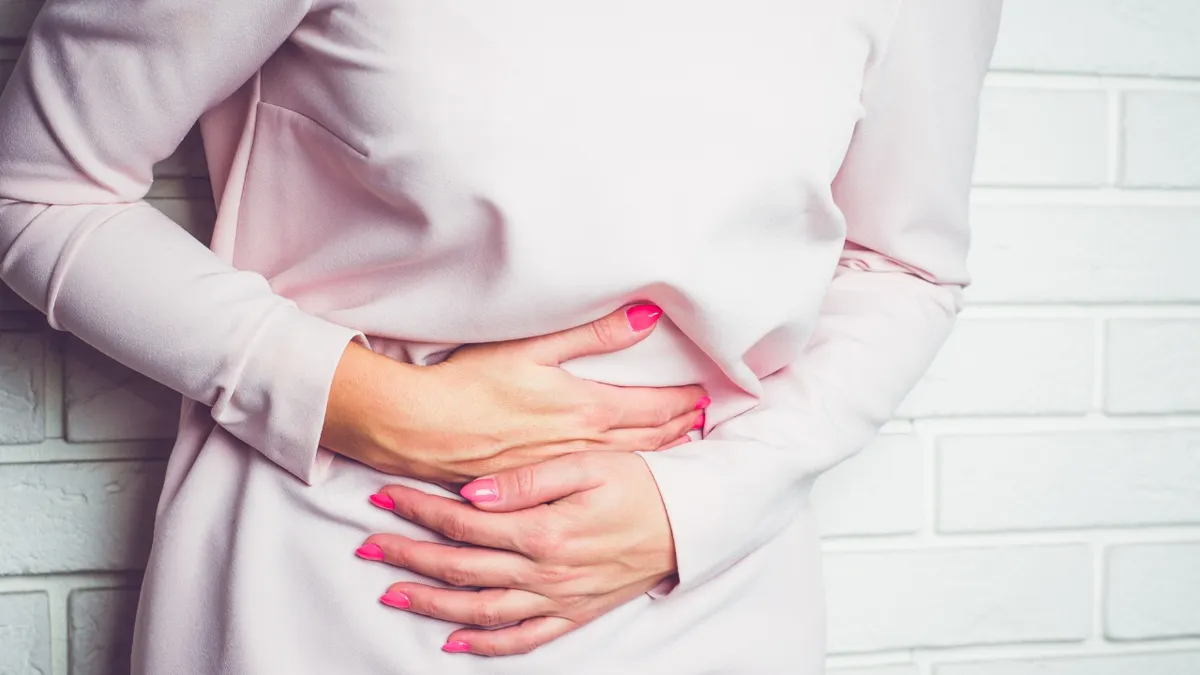 frau mit rosa bluse und rosa nagellack hält sich den bauch weil die gase nicht rauskommen