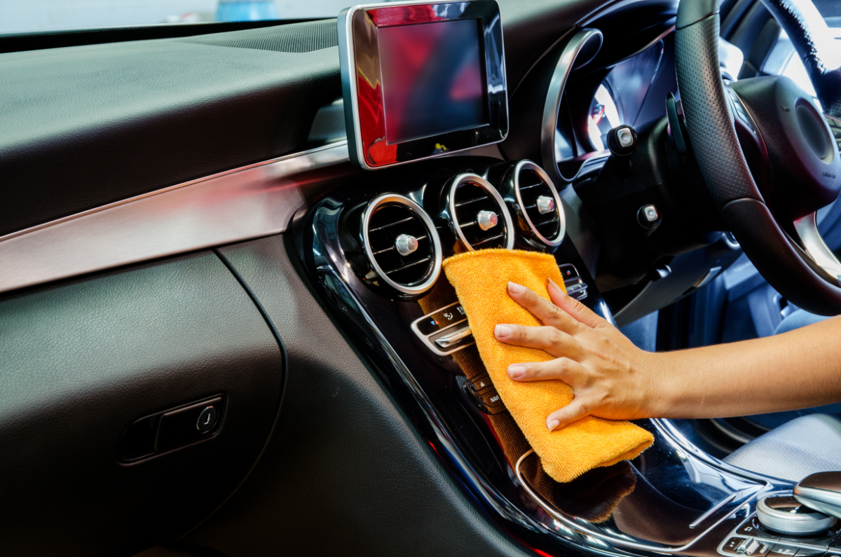 frau reinigt auto konsole mit orangefarbenem mikrofaser handtuch