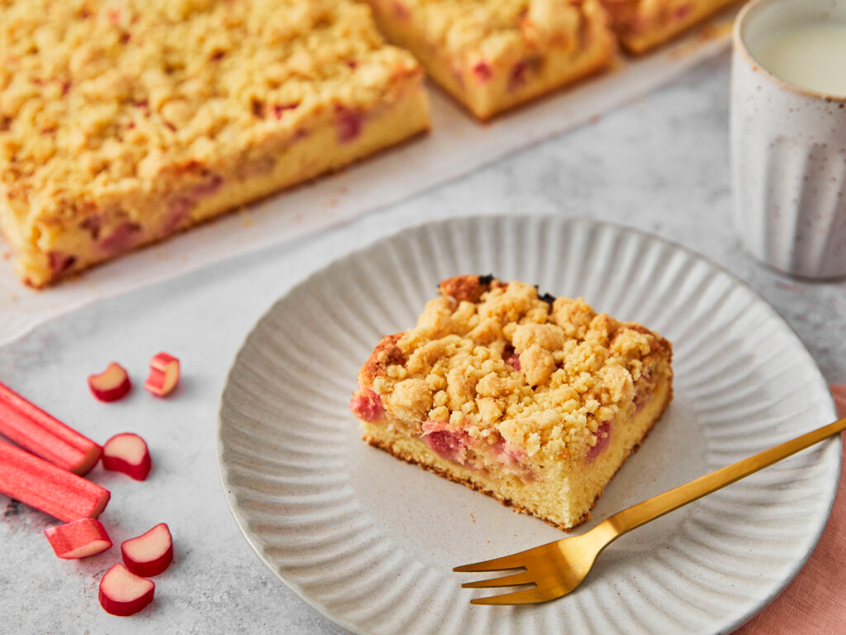 rhabarberkuchen mit streusel im weißen teller mit goldener gabel