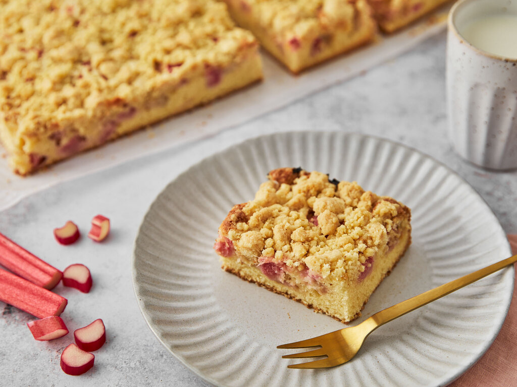 rhabarberkuchen mit streusel im weißen teller mit goldener gabel