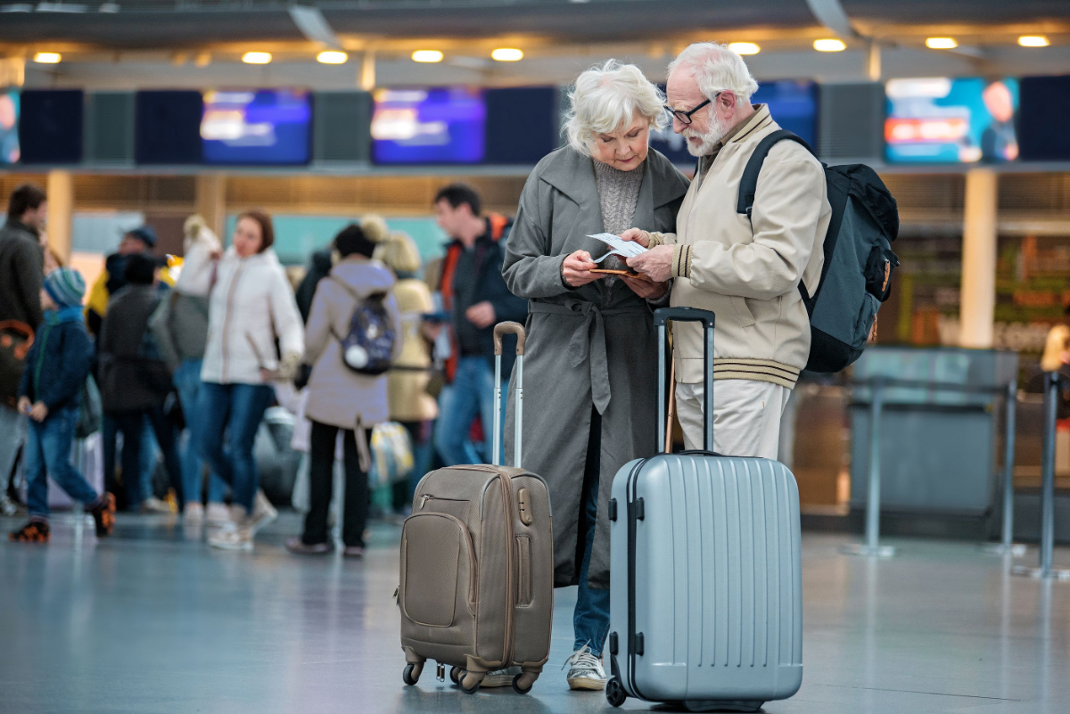 älterer mann und frau am flughafen mit beigen und grauen taschen die ihre reisedokumente betrachten
