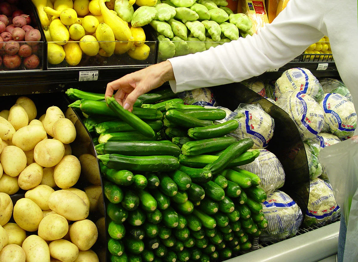 eine frau in weißer bluse wählt in einem supermarkt zucchini aus