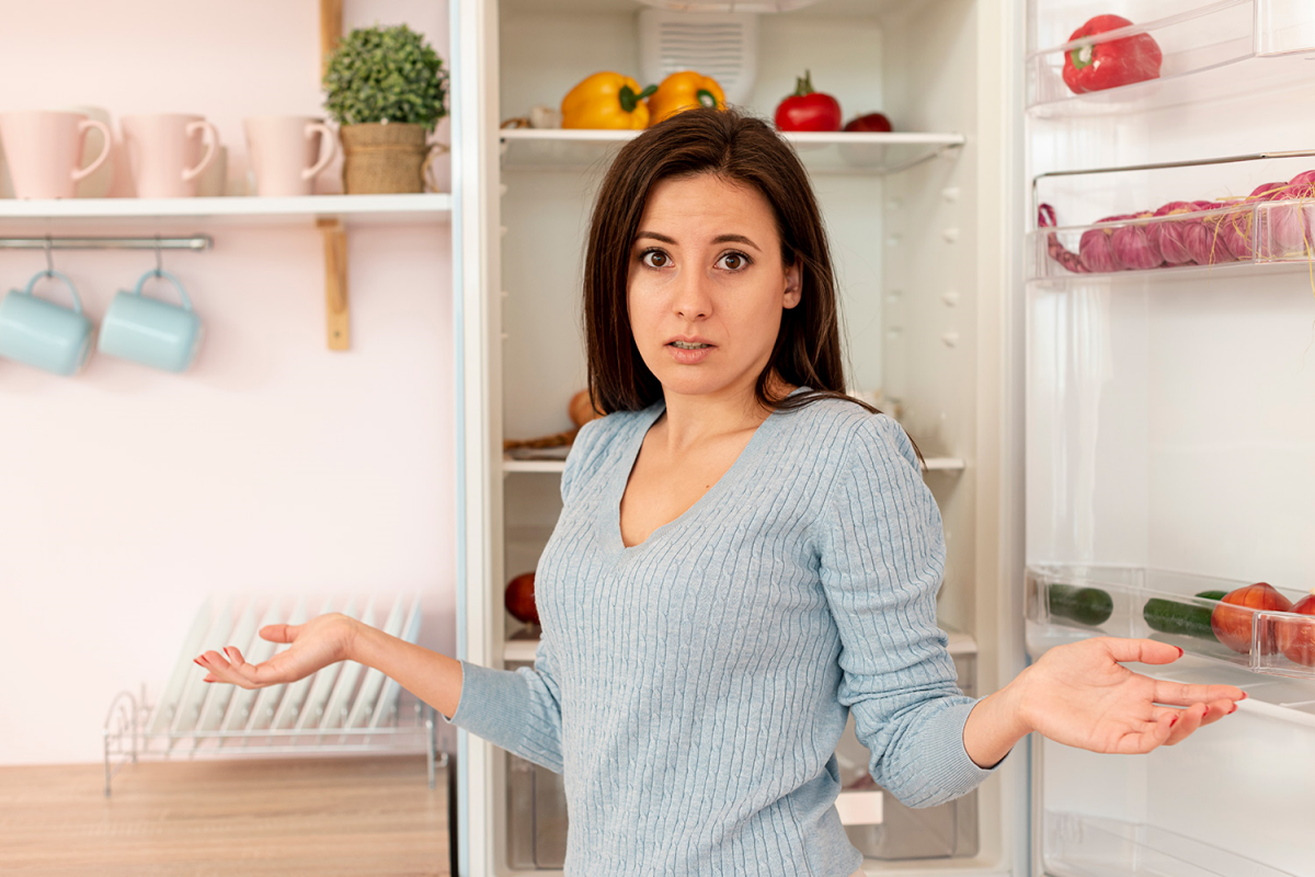 eine frau die neben dem kuehlschrank steht und unzufrieden ist