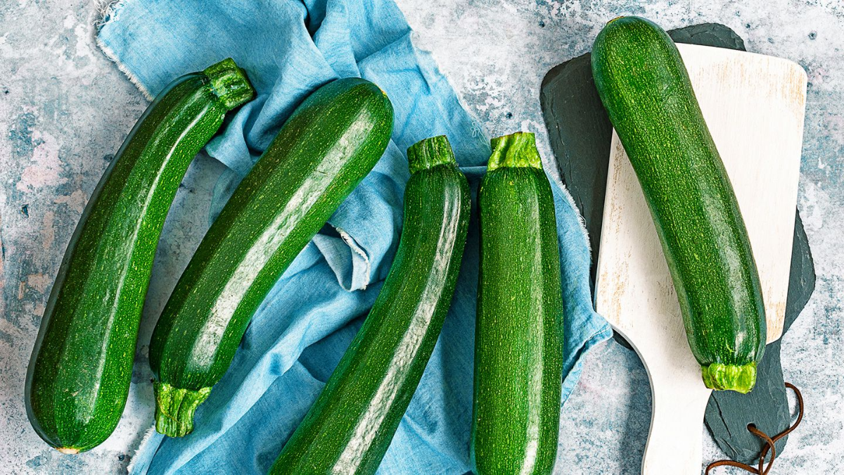 fünf grüne zucchini auf einem blauen tuch und einem weißen schneidebrett