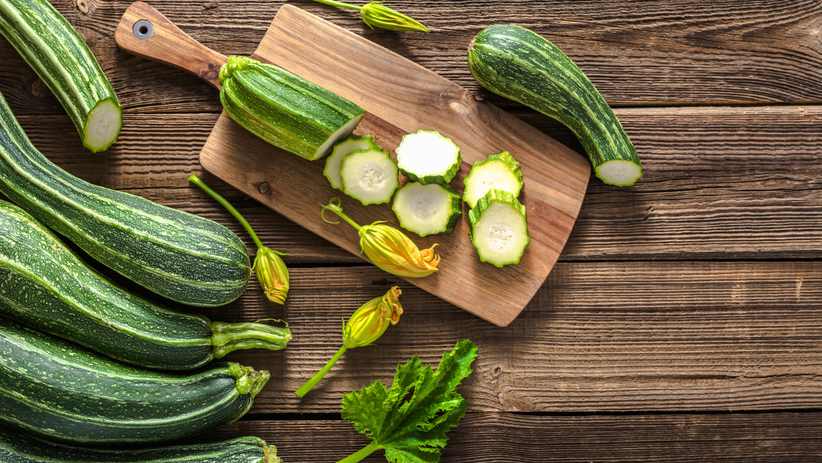 ganze und in scheiben geschnittene zucchini auf einem schneidebrett aus holz