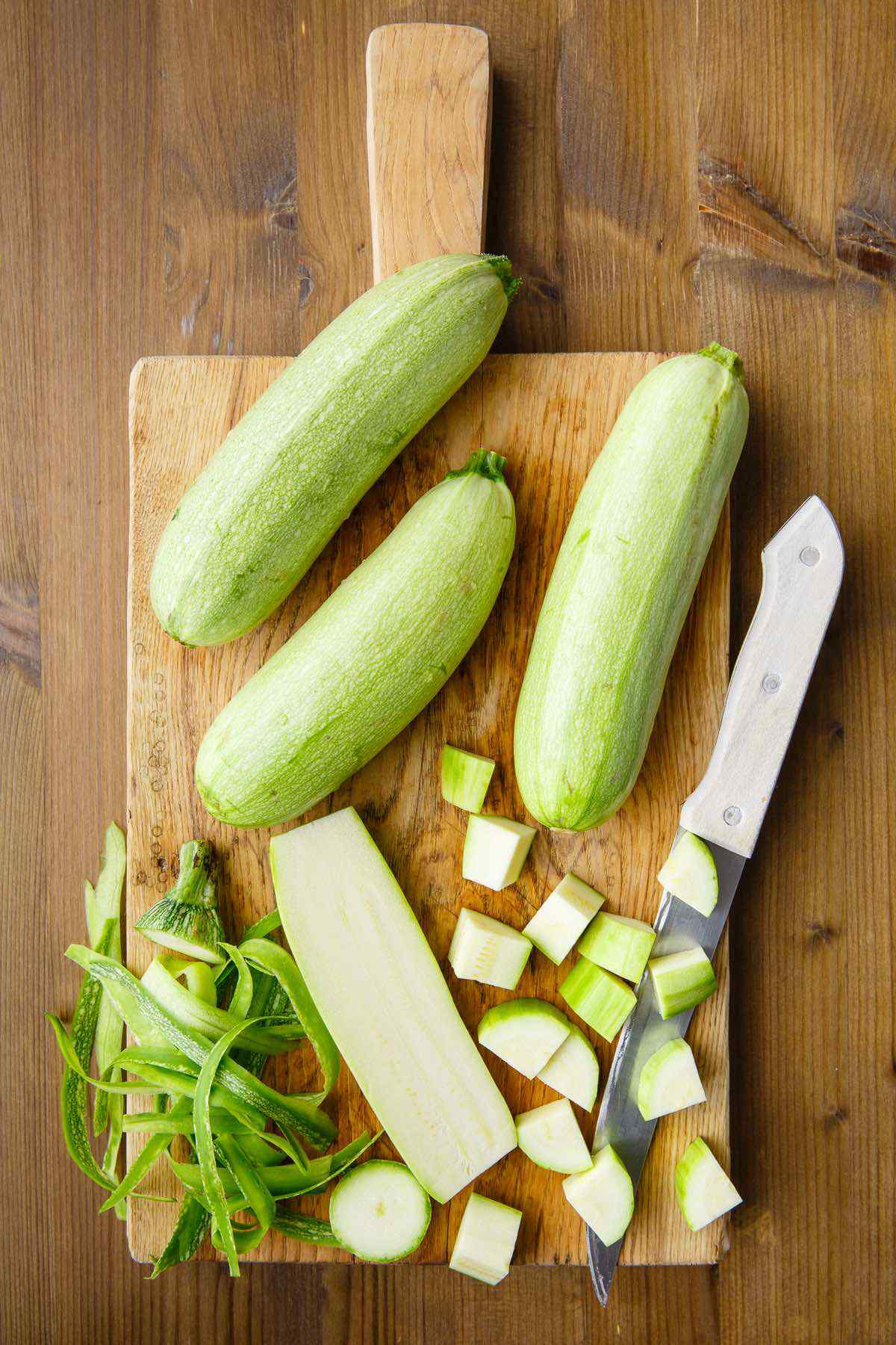 geschnittene und geriebene zucchini für eine zucchini diät auf einem holzbrett und einem weißen messer