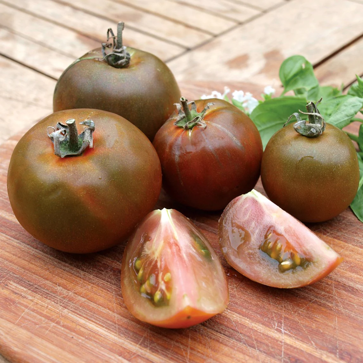 rot schwarze tomaten auf einem hölzernen schneidebrett neben den basilikumblättern