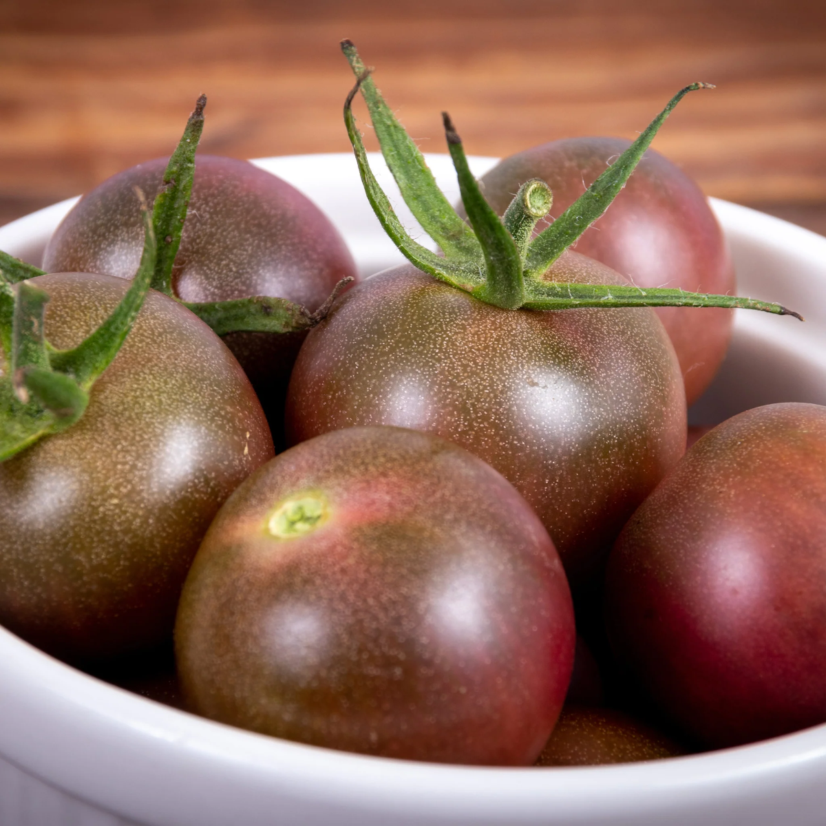 schwarze und rote tomaten mit grünen blättern in weißer schale