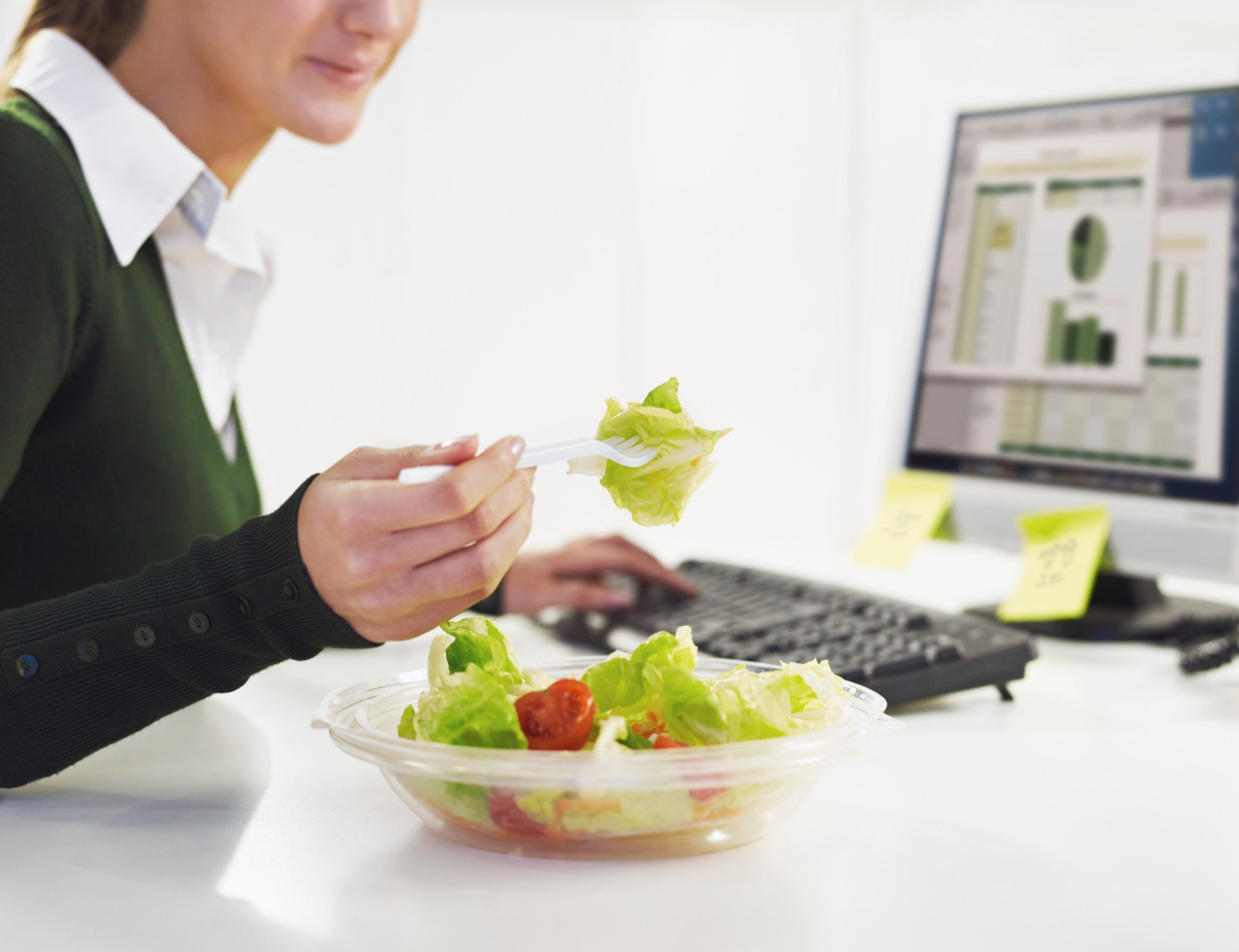 frau mit grünem sweatshirt isst salat im büro vor dem computer
