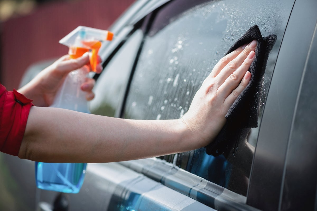 frau mit roter bluse putzt autoscheiben mit spray und mikrofaserhandtuch