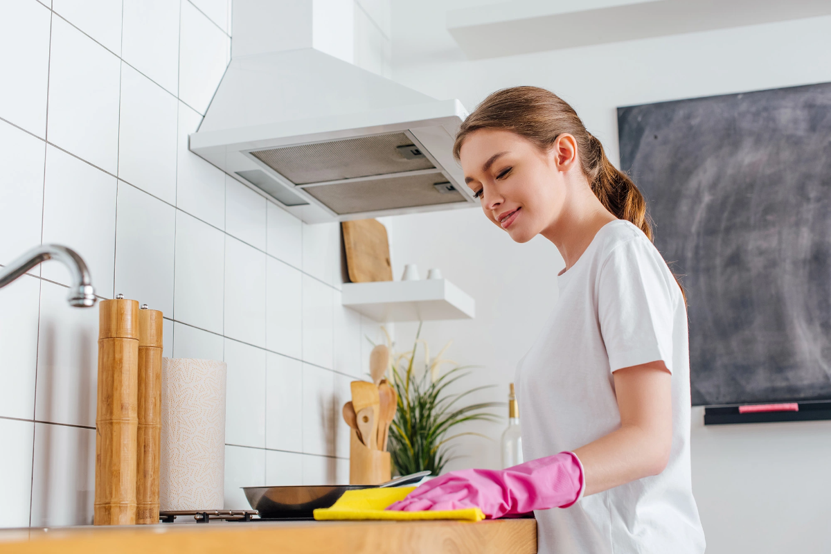frau mit weißem t shirt putzt küche mit gelber tuch und rosa gummihandschuhen um Küchengeräte zu reinigen