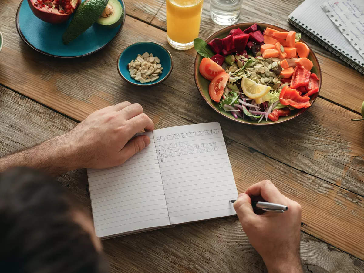 mann schreibt in notizbuch über gesunden lebensstil neben salat und orangensaft