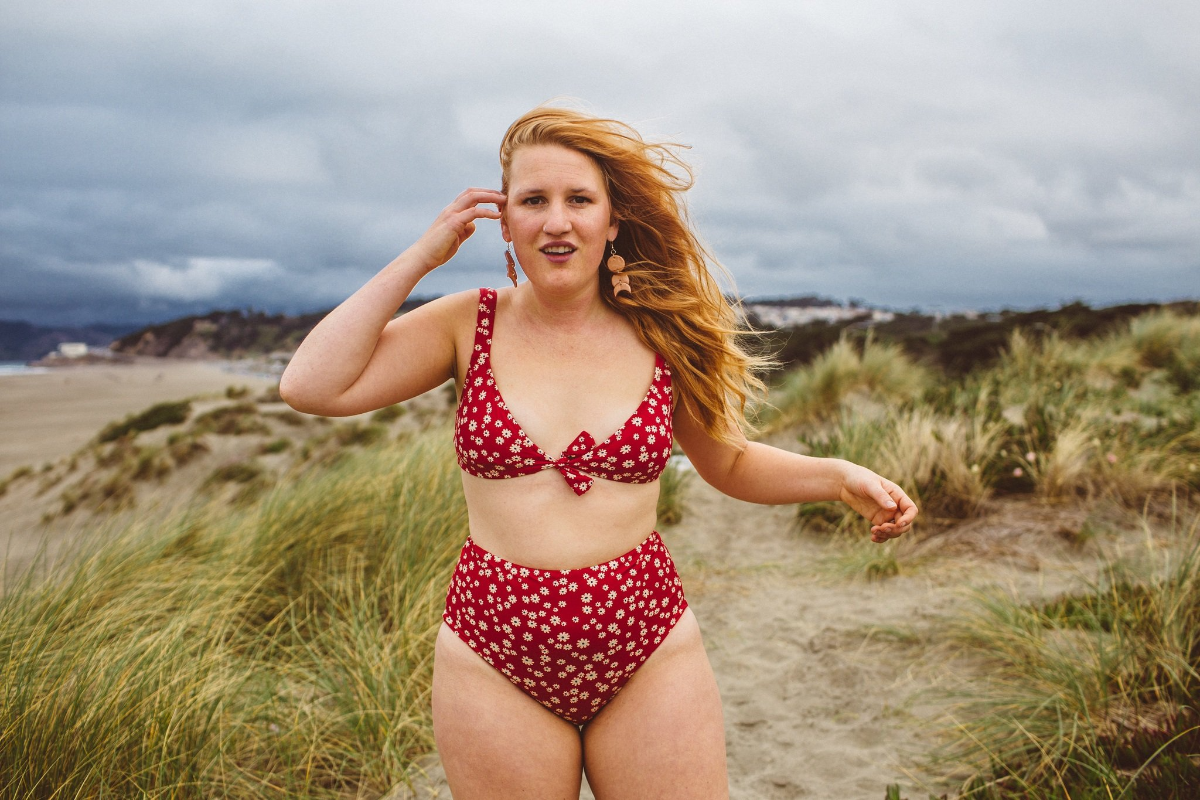 curvy frau mit rotem haar und rotem badeanzug am strand
