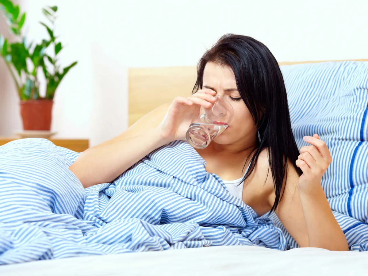 frau mit sommergrippe trinkt wasser während sie im bett liegt
