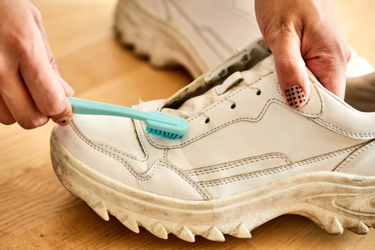 frau mit buntem nagellack entfernt schmutz von weißen schuhen mit blauer zahnbürste