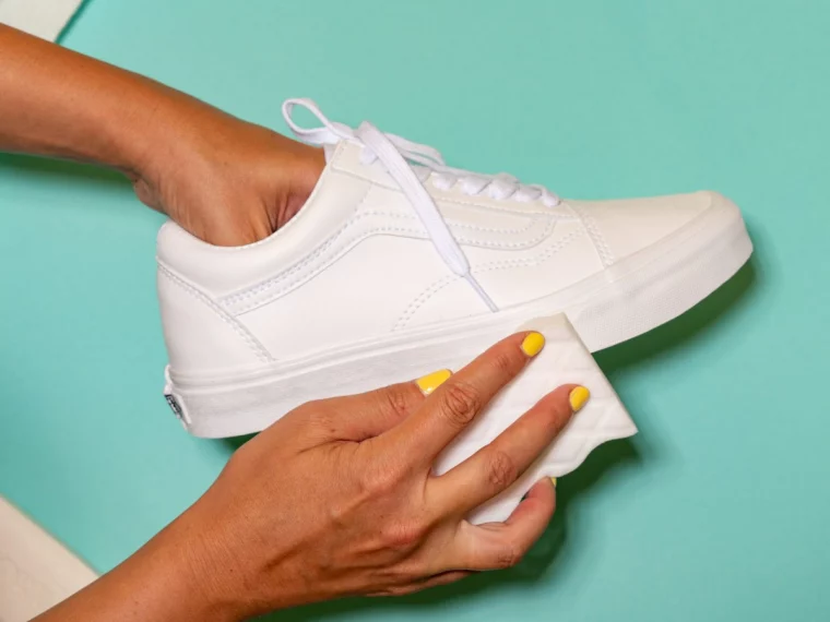 frau mit gelbem nagellack putzt weiße vans schuhe