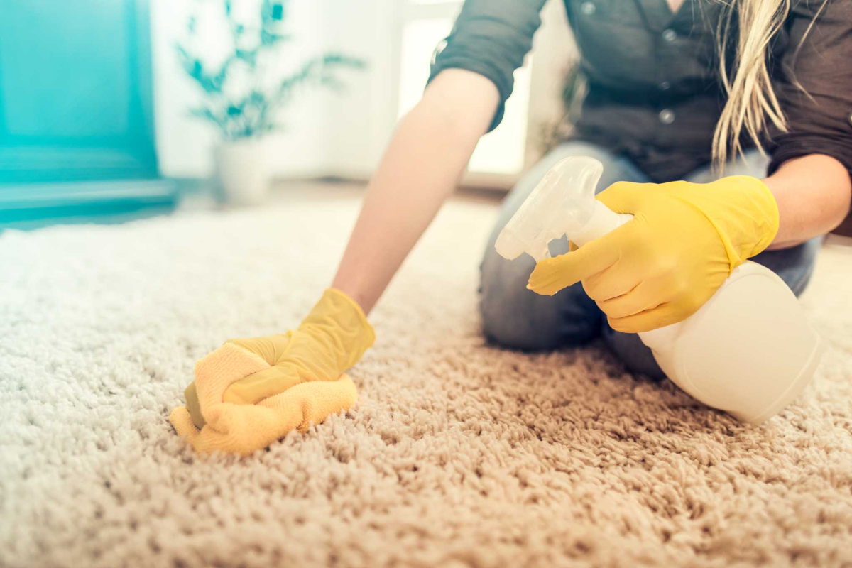frau mit gelben handschuhen reinigt teppich mit hausmitteln