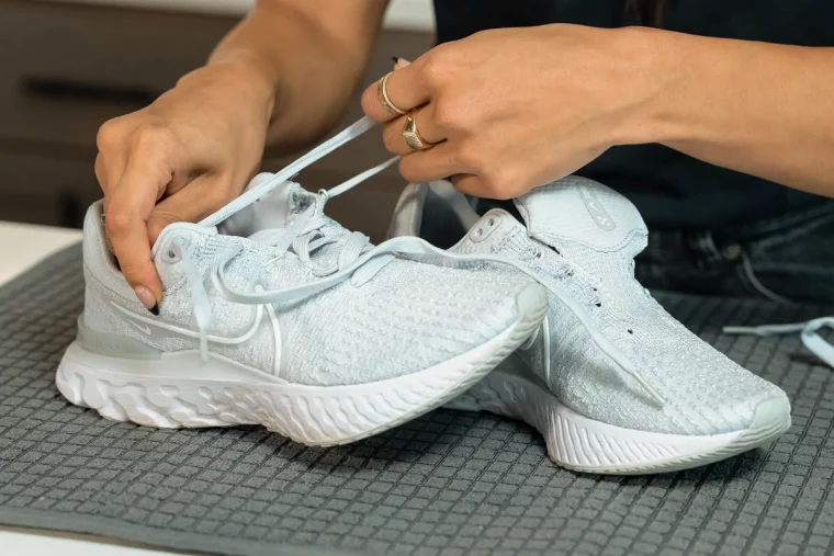 frau mit goldenen ringen beim entfernen der schnürsenkel von weißen nike schuhen
