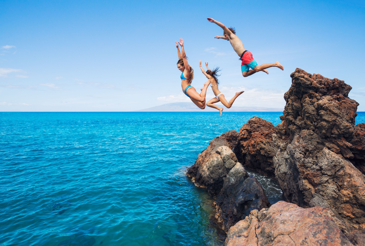 drei menschen springen von einer klippe in den ozean