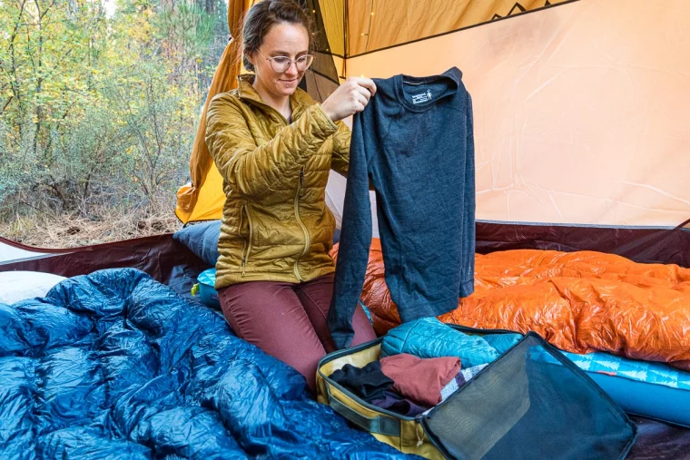 frau mit gelber jacke packt ihre kleidung für das camping im zelt