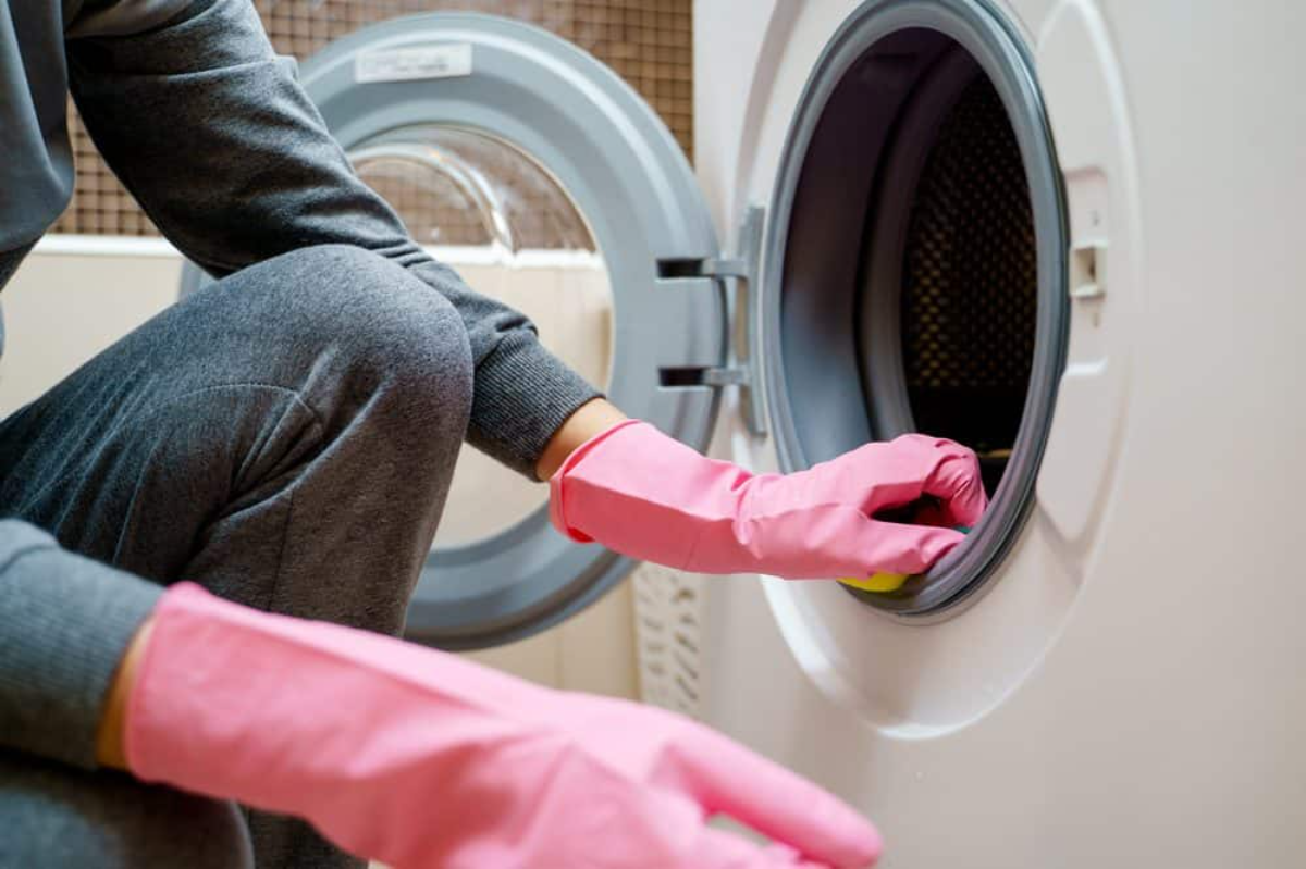 frau mit grauer kleidung und rosa handschuhen beim reinigen der waschmaschine mit hausmitteln