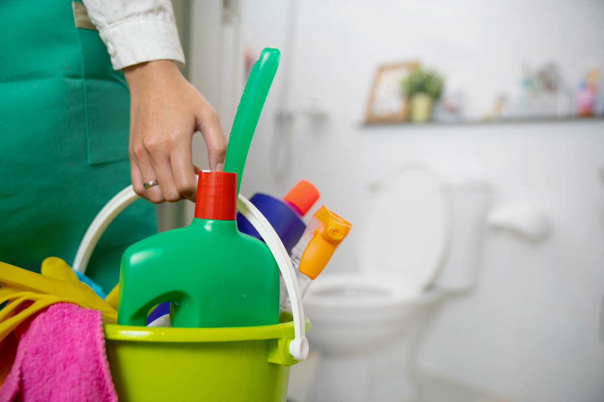 frau mit grüner schürze hält eimer mit reinigungswerkzeugen für die reinigung der toilette