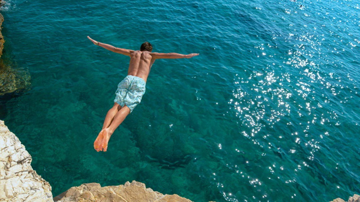 mann mit blauem badeanzug springt von klippe im meer