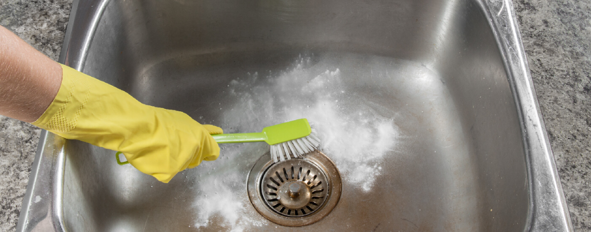 person mit gelben handschuhen beim reinigen des abflusses mit hausmitteln und grüner bürste