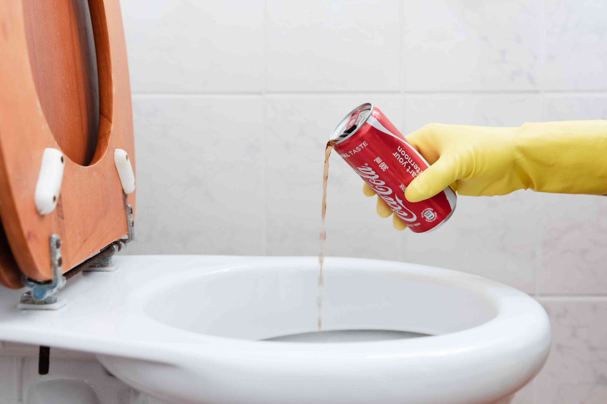 person mit gelben handschuhen, die die toilette mit coca cola reinigt