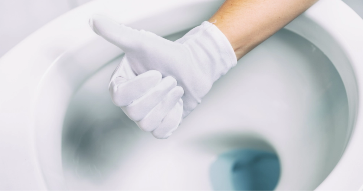 person mit weißem handschuh, die den daumen nach oben hält, vor einer sauberen toilette