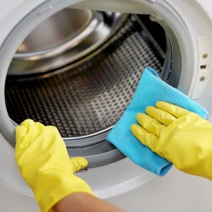 reinigung der waschmaschine mit gelben gummihandschuhen und blauem handtuch
