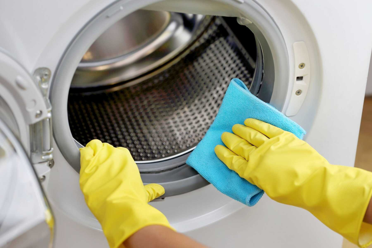 reinigung der waschmaschine mit gelben gummihandschuhen und blauem handtuch
