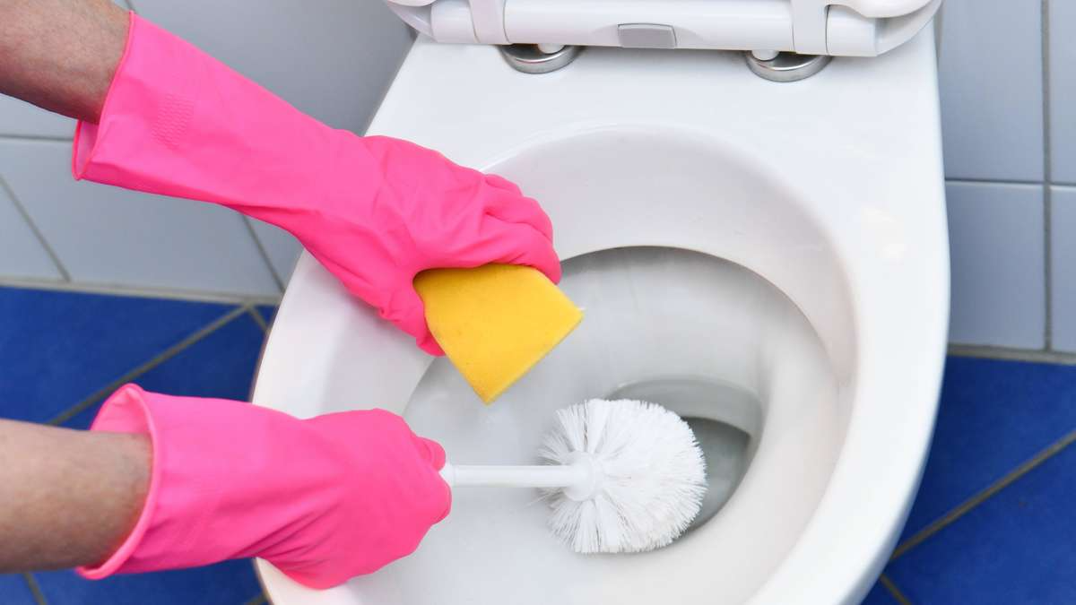 reinigung der weißen toilette mit gelbem schwamm und rosa handschuhen