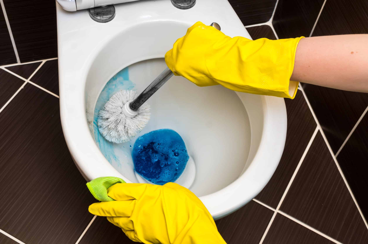 urinstein in der toilette mit gelben handschuhen und blauem reinigungsmittel entfernen