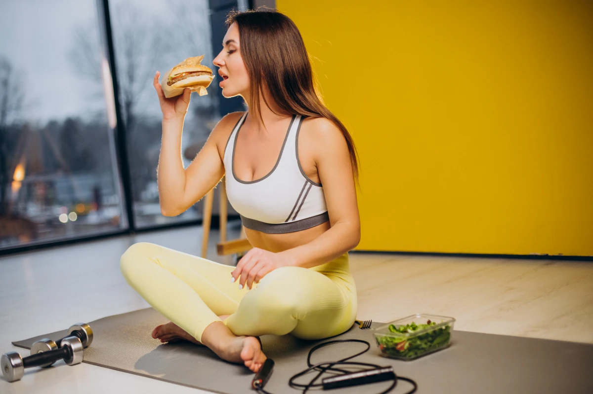 auf leeren magen trainieren frau isst hamburger beim training