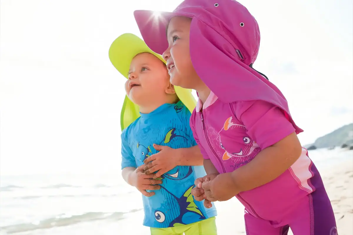 beste stoffe fuer sommer babys zwei kinder am strand mit speziellen huetchen sonnenschutz