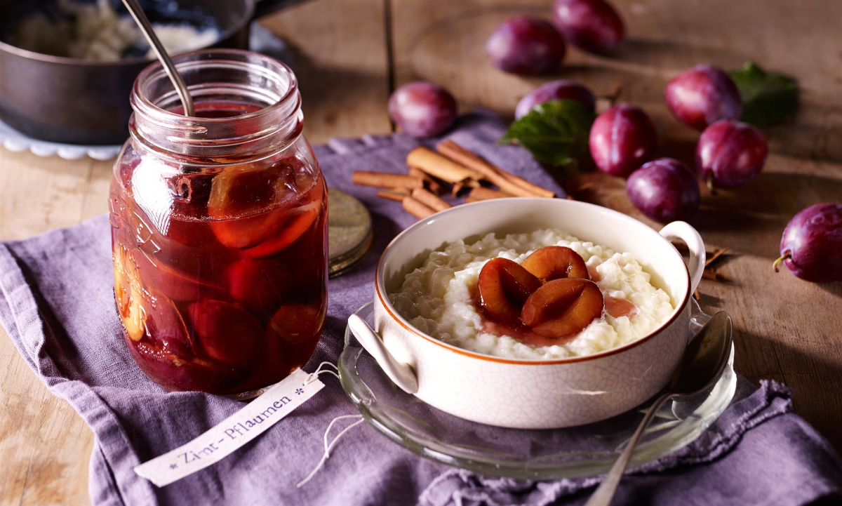 eingelegte pflaumen im glas neben einem dessert mit pflaumen und zimt