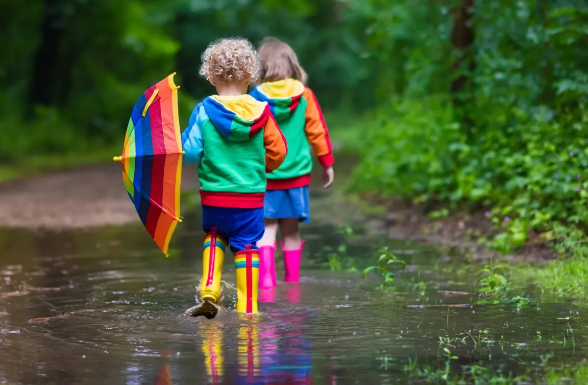 kinder spielen outdoor im regen bunte kleidung gummistiefel regenschirm