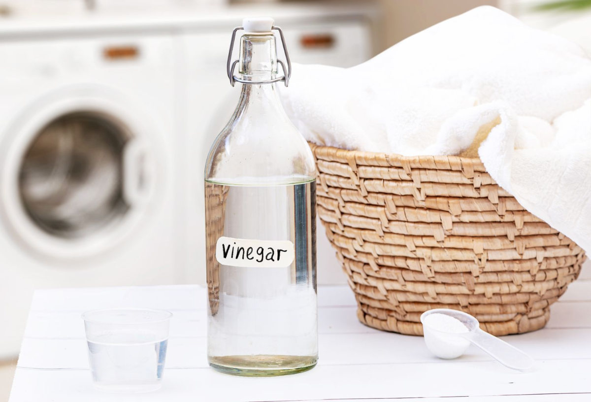 flasche mit essig neben dem korb mit weißer wäsche neben der waschmaschine