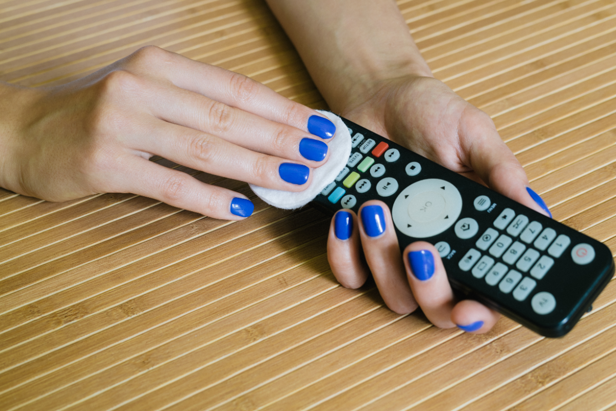 frau mit blauem nagellack beim reinigen der tv fernbedienung