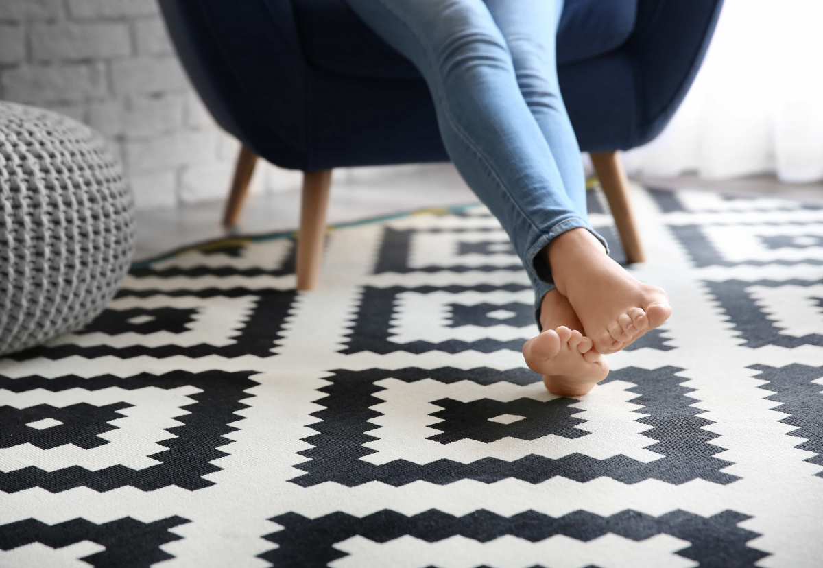 frau mit blauen jeans sitzt auf blauer couch mit nackten füßen auf teppich