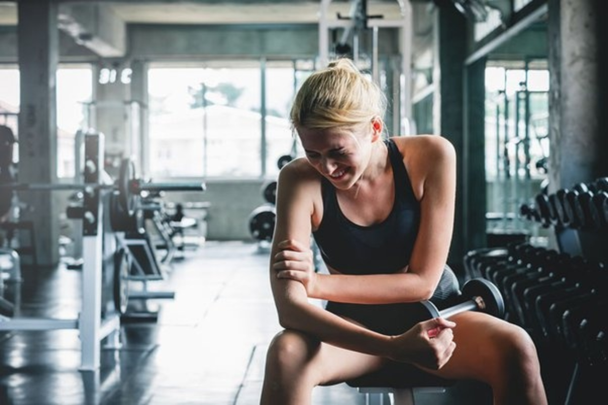 frau mit blondem haar sitzt im fitnessstudio und hat muskelkater