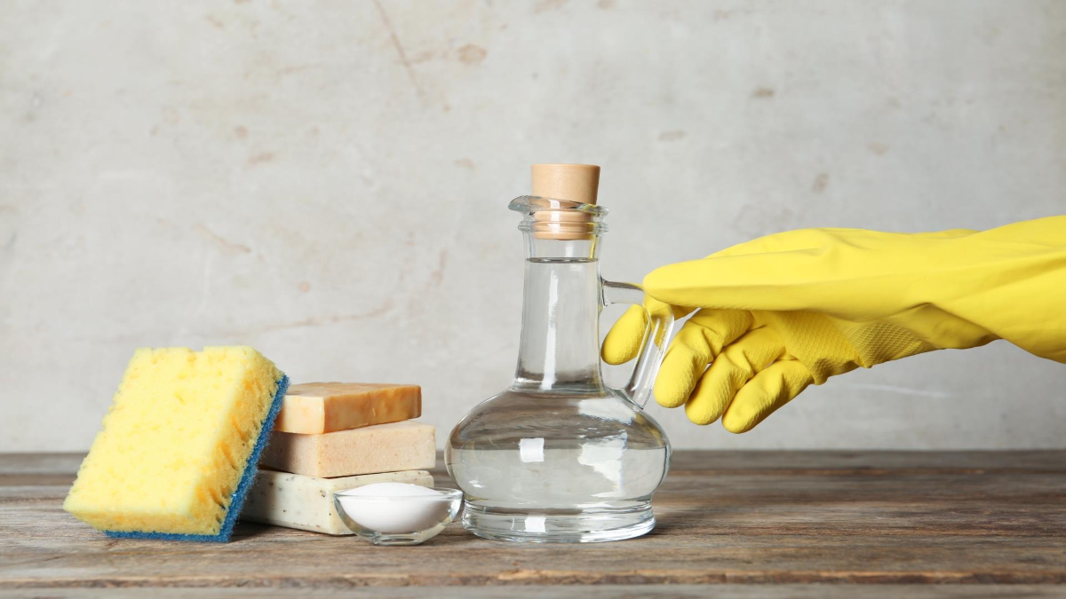person hält essig mit gelbem gummihandschuh zum reinigen