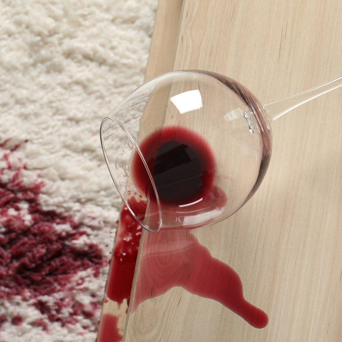 ein glas mit rotwein ist auf den tisch gefallen und der wein steht auf dem weißen teppich