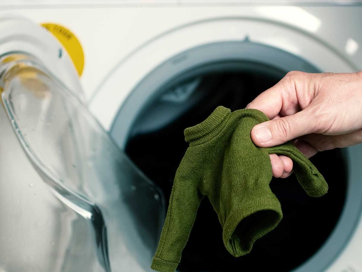 person, die einen kleinen grünen pullover hält, der in der waschmaschine geschrumpft ist
