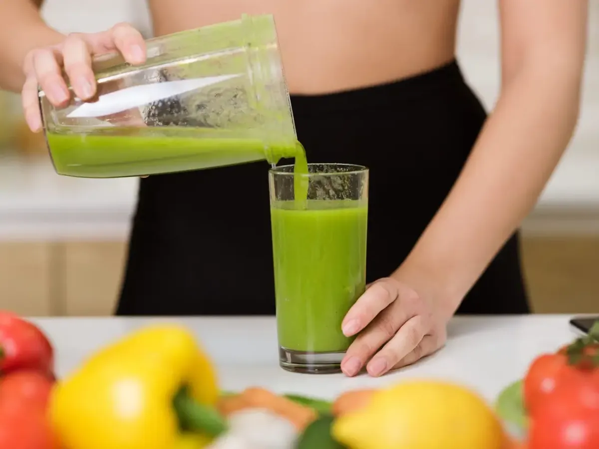 frau schenkt gruenen saft in ein glas ein