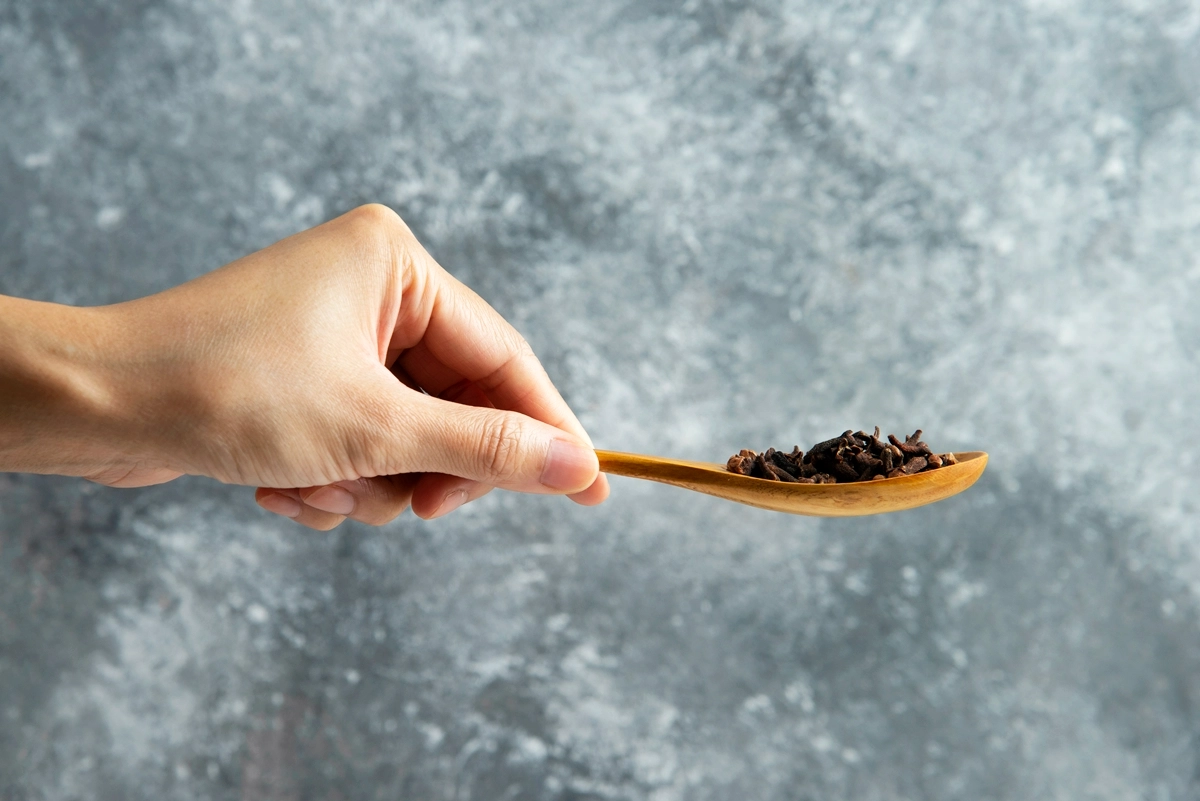 nigella seeds in hoelzernem loeffel hand grauer hintergund