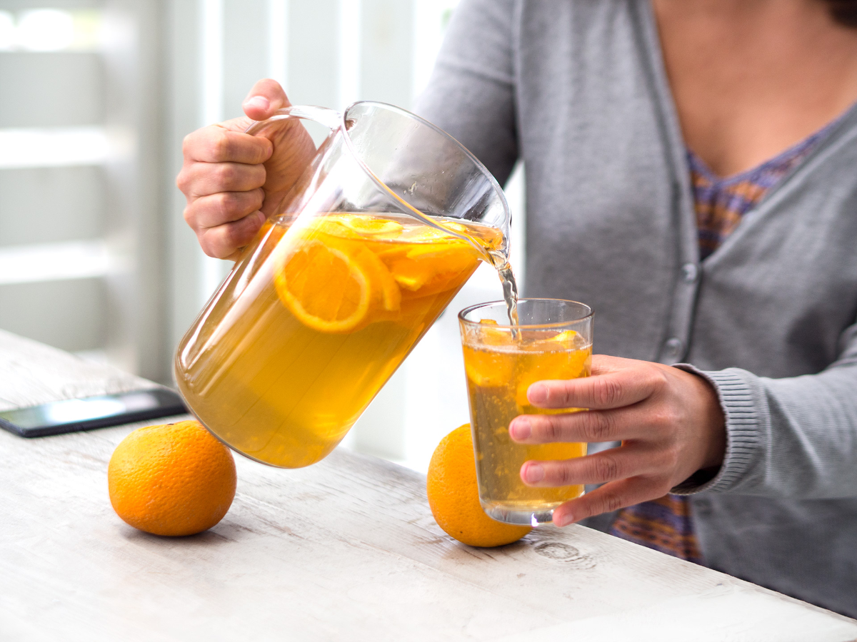 frau gießt kombucha mit orangen in ein glas
