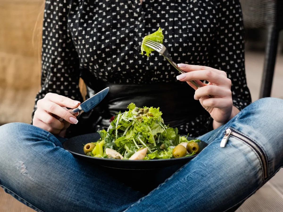 frau sitzt auf dem boden und isst gruenen salat